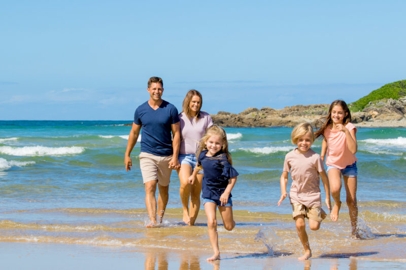 Young family having fun at the beach opposite BIG4 Park Beach Holiday Park with kids running in waves