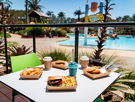 Fish and chips, burgers, coffees and slushy sitting on table overlooking pool at BIG4 Park Beach Holiday park